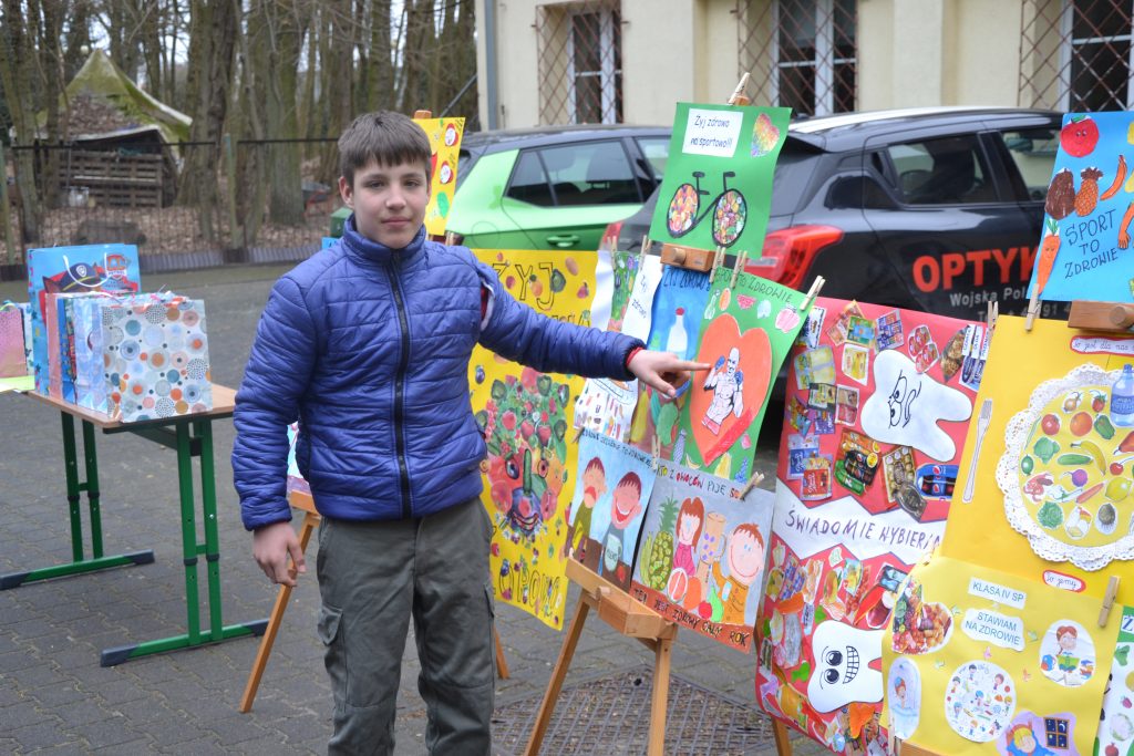 młody chłopak stojący obok wystawy obrazów.