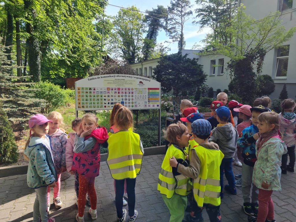 grupa dzieci w żółtych kamizelkach stojących przed szyldem.