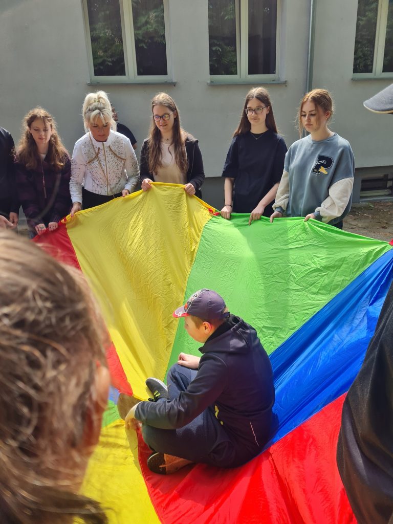 grupa ludzi stojących wokół tęczowego latawca.