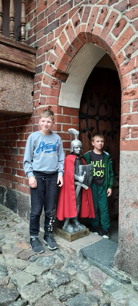 dwóch młodych chłopców stojących obok posągu rycerza.