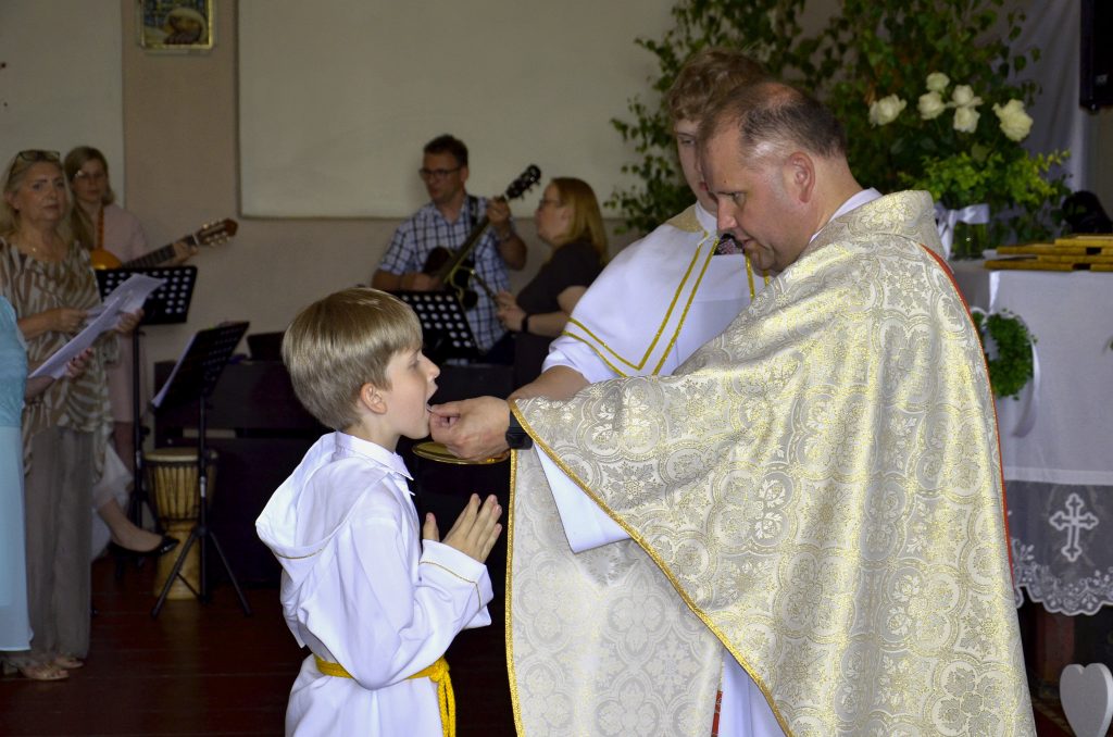 mały chłopiec w stroju księdza ściskający dłoń księdza.