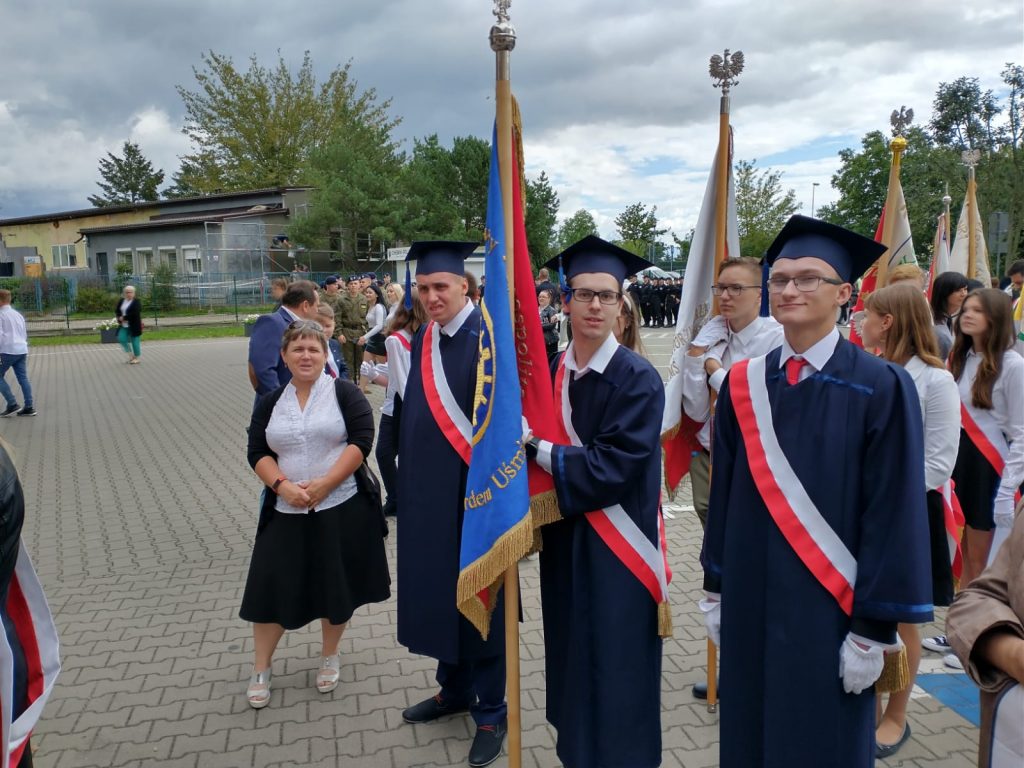 grupa mężczyzn stojących obok siebie przed flagą.