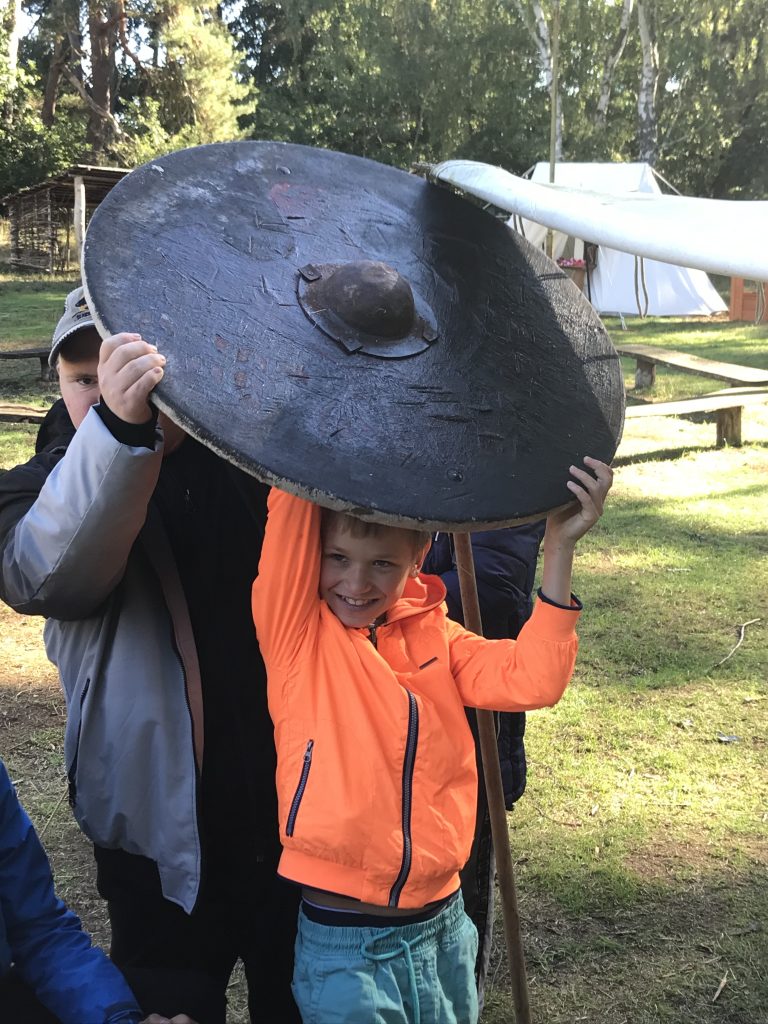 młody chłopiec trzymający duży metalowy przedmiot na czubku głowy.