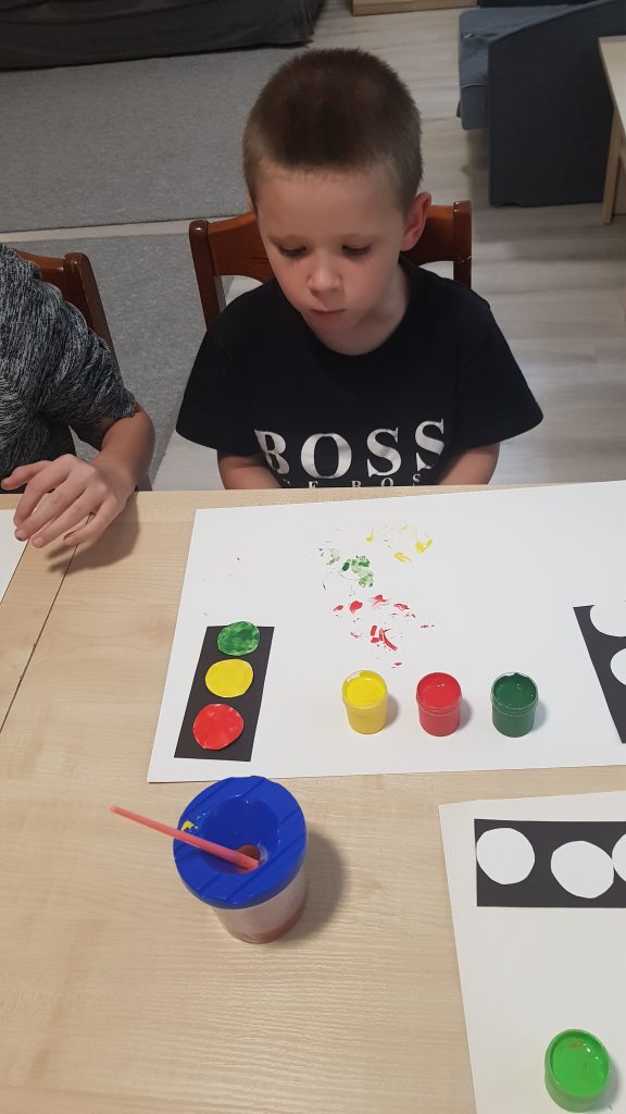 dwoje dzieci siedzi przy stole z farbą i papierem.