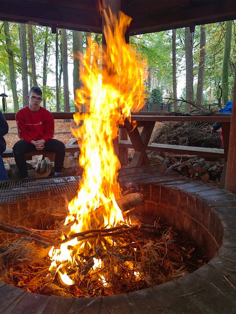 dwóch mężczyzn siedzi wokół ogniska w lesie.