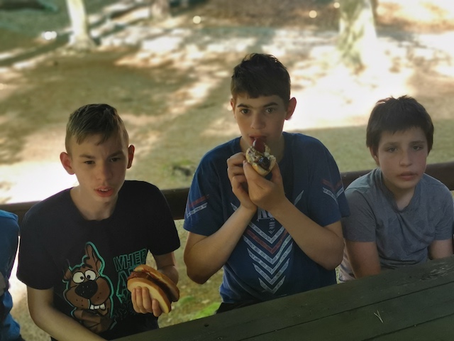 grupa chłopców siedzących na ławce i jedzących jedzenie.
