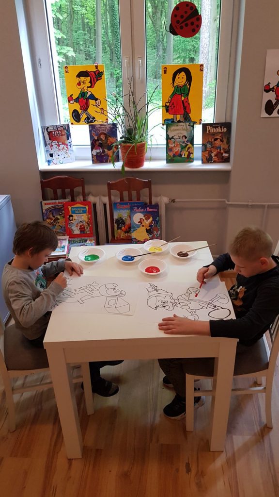 dwóch młodych chłopców siedzących przy stole z rysunkiem.