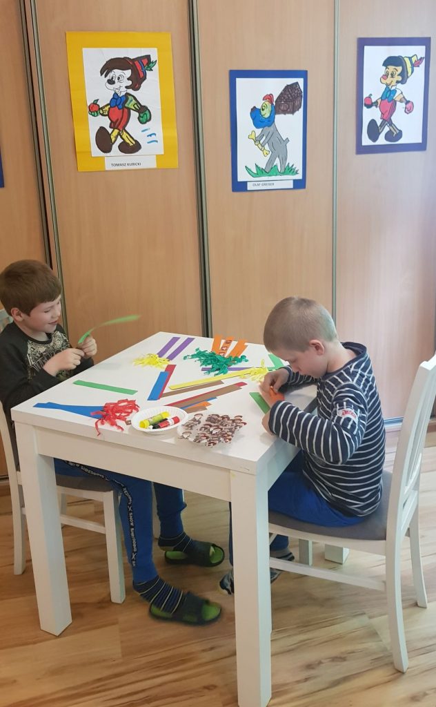 dwóch młodych chłopców siedzących przy stole z obrazami.