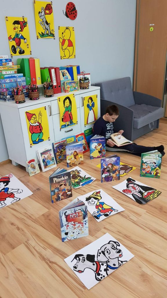 młody chłopiec siedzący na podłodze otoczony książkami dla dzieci.