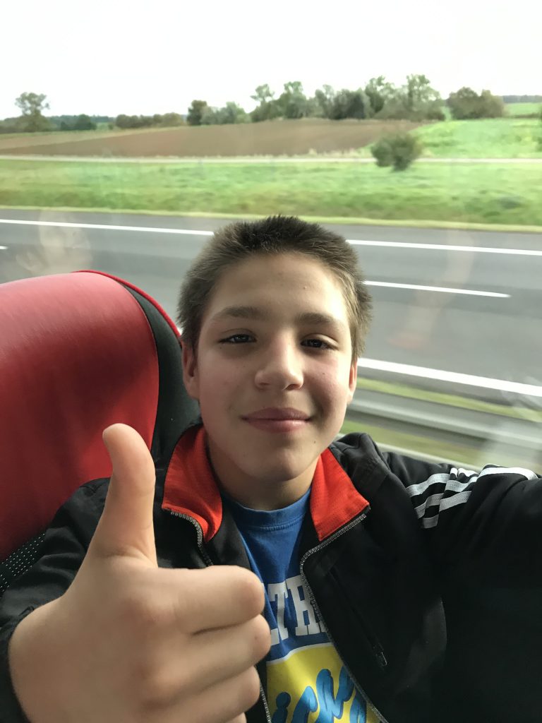 młody chłopak podnoszący kciuki do góry podczas jazdy autobusem.