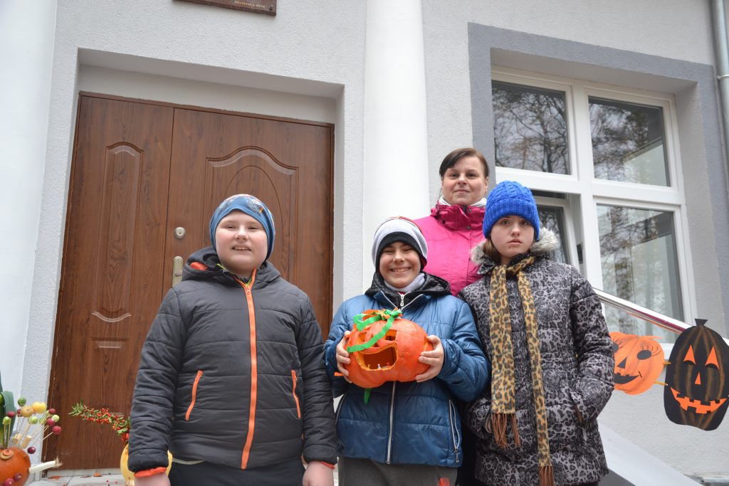 grupa dzieci trzyma dynie przed domem.