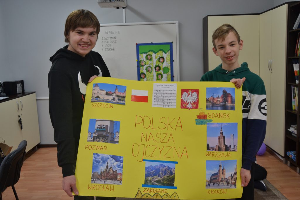 dwóch chłopców trzyma żółty znak z obrazkami.
