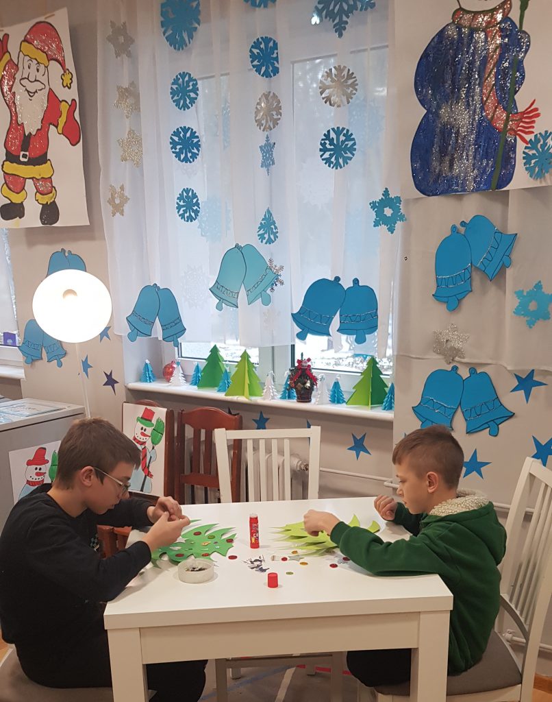 dwóch chłopców siedzących przy stole bawiących się papierowymi dekoracjami.