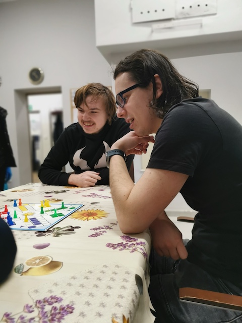 dwie osoby siedzące przy stole i grające w grę planszową.