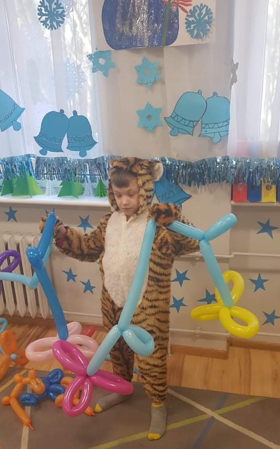 mały chłopiec w kostiumie tygrysa stojący obok pęku balonów.