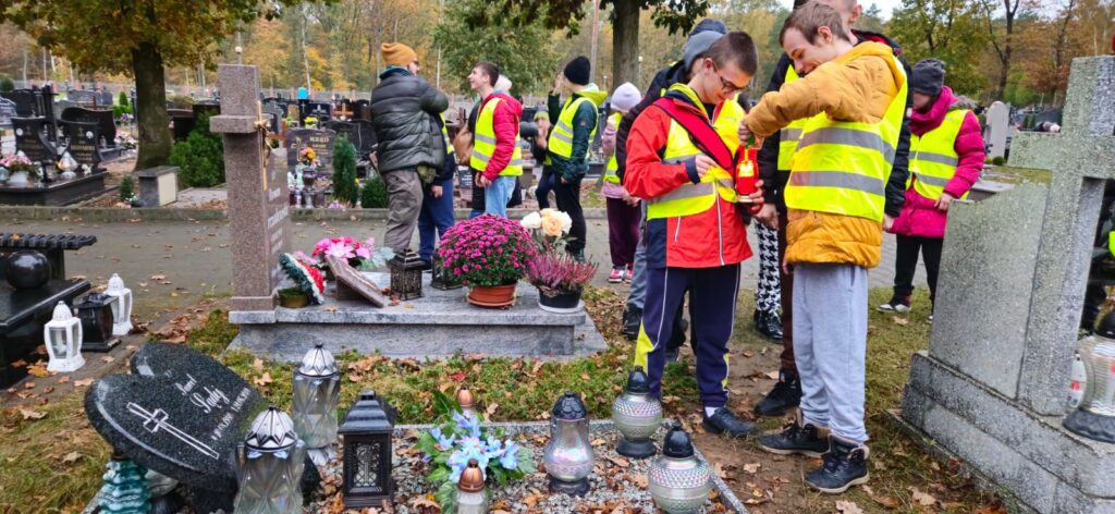 Uczniowie zapalają znicze na cmentarzu 